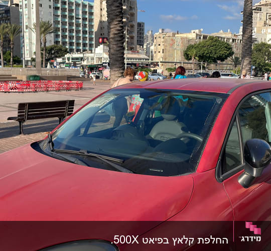 מכונית אדומה חונה ליד מדרכה עם עצי דקל ברקע